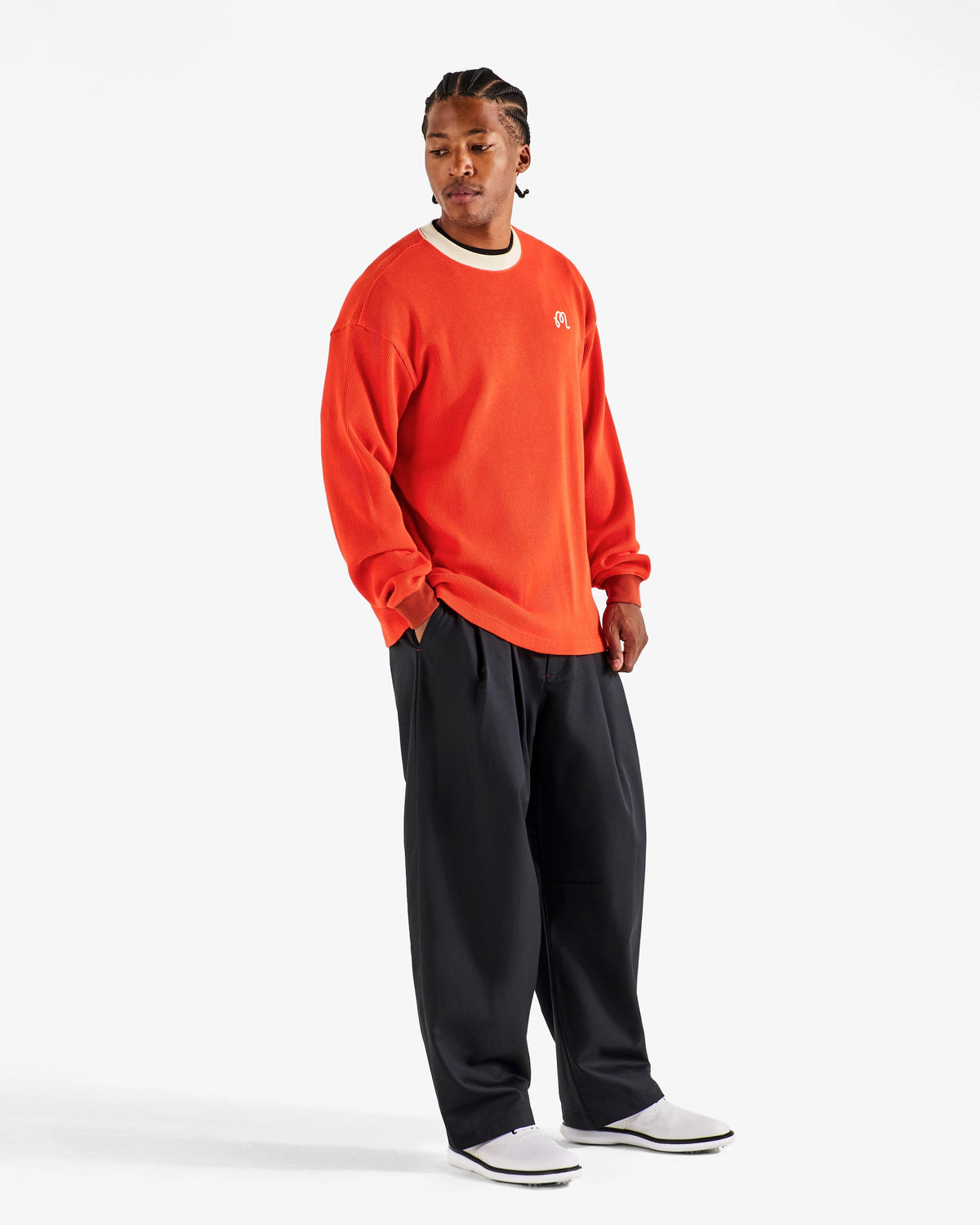 Full length front view of a model in the Malbon Golf Gorse Heritage Long Sleeve orange red, styled with black wide leg trousers and white golf shoes