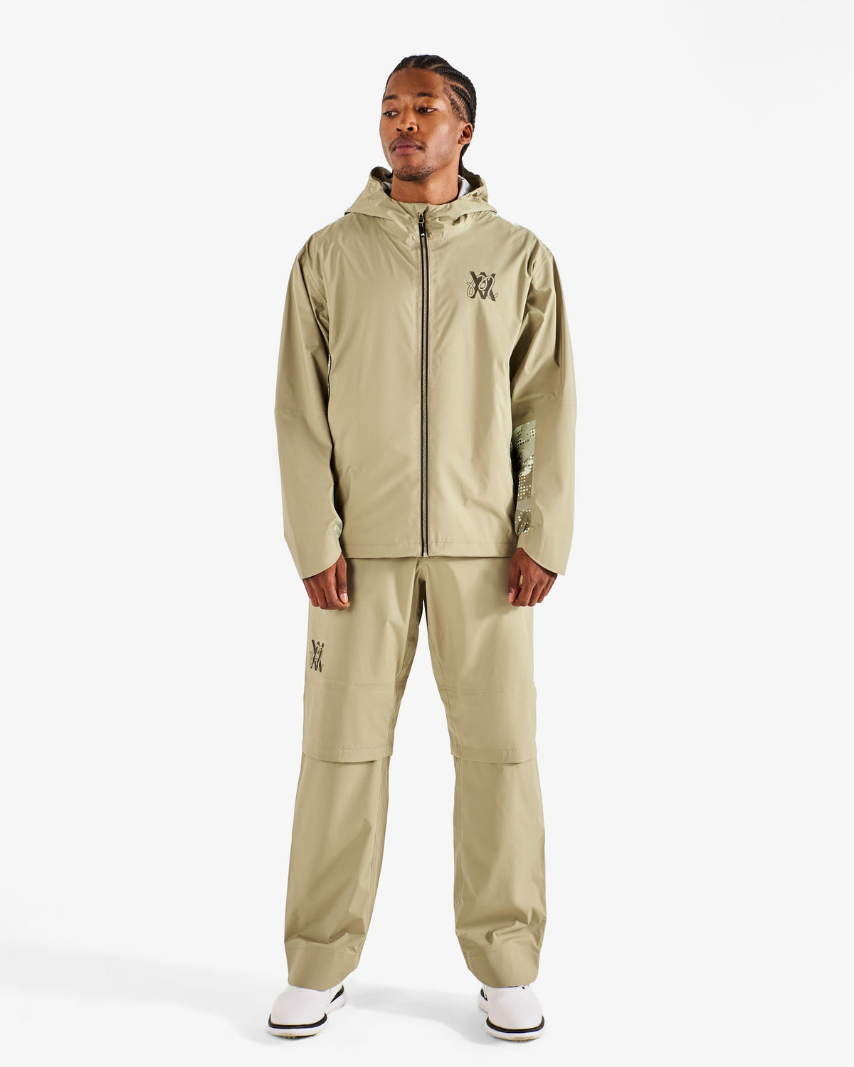 Malbon Golf x Daniel Arsham Cloudburst Rain Jacket – Dune worn on model — beige hooded full-zip rain jacket with dotted-camo panels, Gallery Streetwear Canada