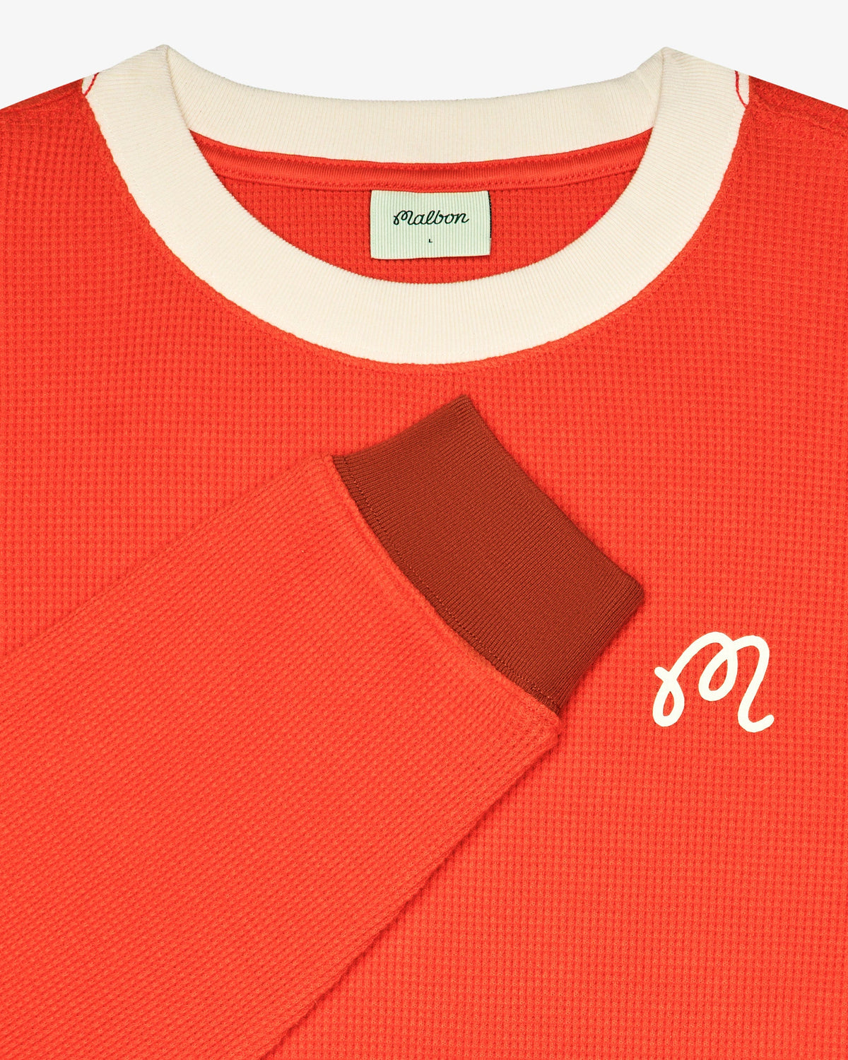 Detail of the Malbon Golf Gorse Heritage Long Sleeve showing waffle knit texture, cream ribbed collar, rust ribbed cuff, woven Malbon label and embroidered M script