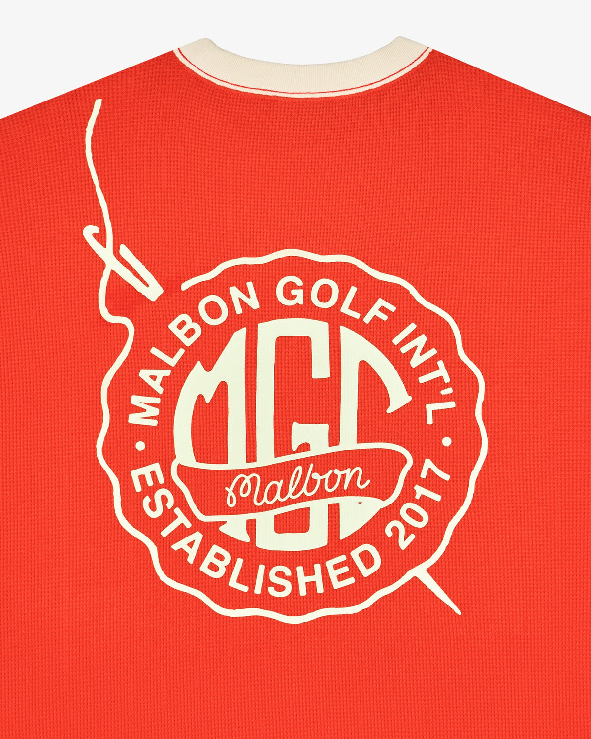 Close up of the back graphic on the Malbon Golf Gorse Heritage Long Sleeve, reading Malbon Golf Int'l MGC Established 2017 in cream print on orange red waffle knit